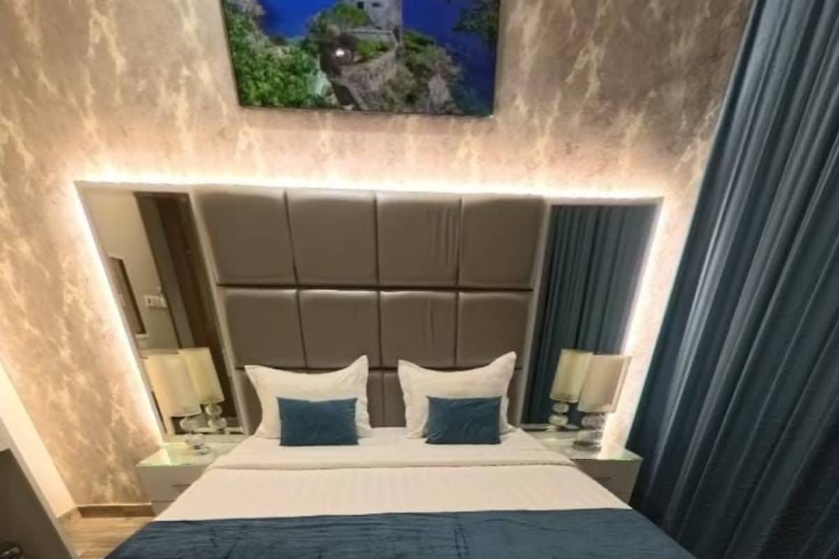 Habitación de hotel con una cama grande, cabecero, mesitas de noche y televisión montada en la pared.