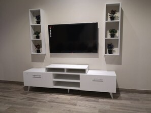 Un mueble blanco de entretenimiento con un televisor de pantalla plana montado encima, flanqueado por dos estanterías blancas con plantas en macetas.