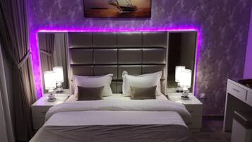 Una habitación de hotel con una cama grande, dos mesitas de noche con lámparas, un cabecero y un cuadro sobre la cama.