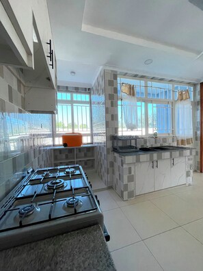 A modern kitchen with a gas stove, a sink, and a window with curtains. - 5 BEDROOM MODERN  VILLA IN DIANI MOMBASA KENYA. 10 MINUTES WALK TO BEACH (Diani Beach)