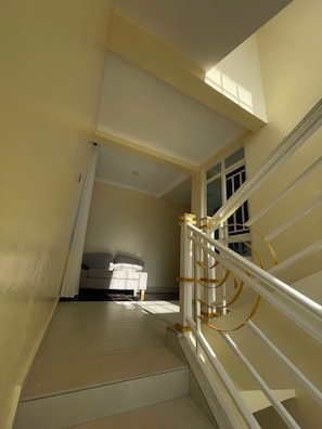A staircase with a white railing and a view of a room with a bed and a window. - 5 BEDROOM MODERN  VILLA IN DIANI MOMBASA KENYA. 10 MINUTES WALK TO BEACH (Diani Beach)