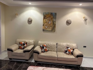 Un salon avec deux canapés en cuir, des coussins à motifs, un sol en marbre et un tableau représentant un lion accroché au mur.