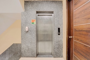 An elevator with a fire safety sign, a wall-mounted intercom, and a door with a handle. - Hotel O IGI Airport Mahipalpur (New Delhi)