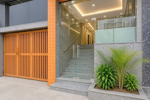 A modern building entrance with a large orange door, a glass staircase, and a small planter with green plants. - Hotel O IGI Airport Mahipalpur (New Delhi)