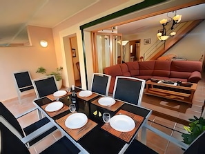 A dining area with a glass table, black chairs, and a red sofa in the background. - Holiday Home 'Els Pins' with Private Terrace, Wi-Fi and Air Conditioning (Port d'Alcúdia)