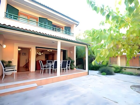 A two-story house with a covered patio, a dining area with chairs and a table, and a staircase leading to an upper floor. - Holiday Home 'Els Pins' with Private Terrace, Wi-Fi and Air Conditioning (Port d'Alcúdia)