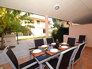 A dining area with tables and chairs, a potted plant, and a view of buildings outside. - Holiday Home 'Els Pins' with Private Terrace, Wi-Fi and Air Conditioning (Port d'Alcúdia)