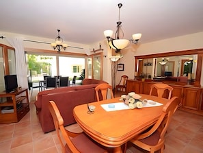 A dining area with a wooden table and chairs, a sofa, and a chandelier. - Holiday Home 'Els Pins' with Private Terrace, Wi-Fi and Air Conditioning (Port d'Alcúdia)