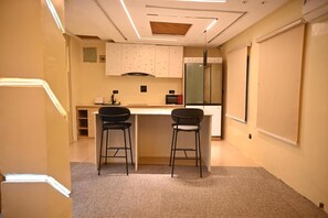 A small kitchenette with a refrigerator, a microwave, and a stove. There are two stools and a small table.