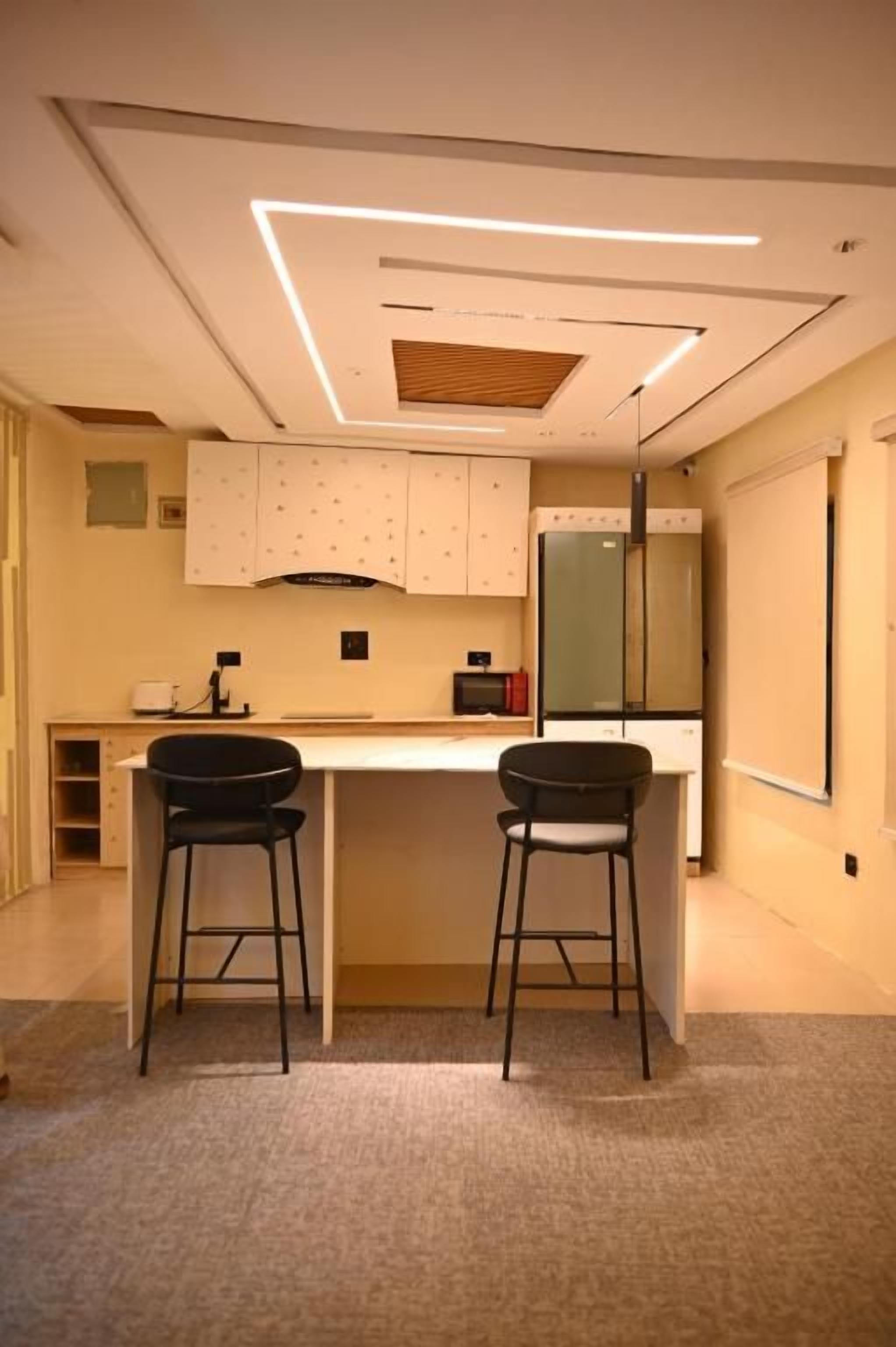 A modern kitchen with a central island, two bar stools, and a built-in refrigerator.