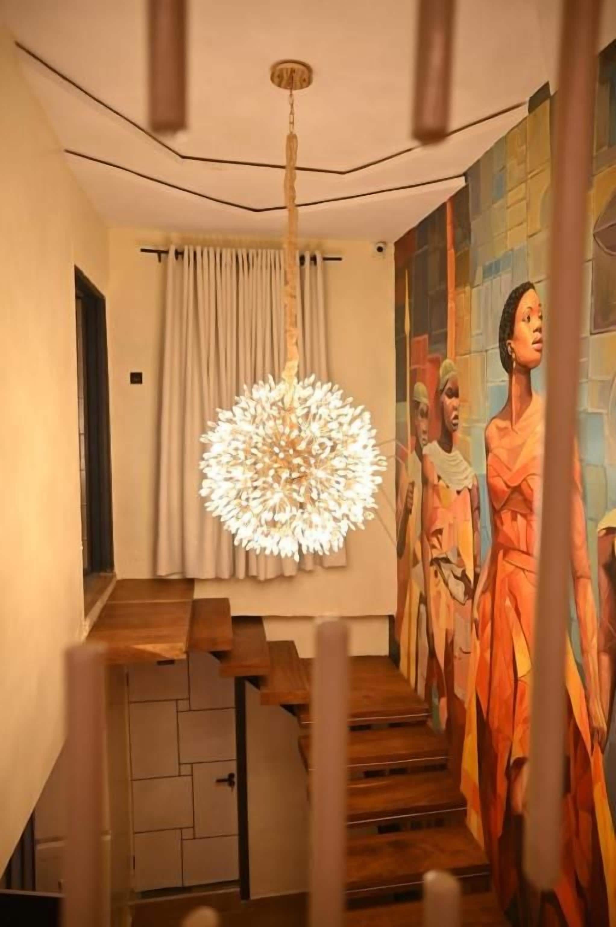 A staircase with a modern chandelier, a mural on the wall, and a wooden floor.