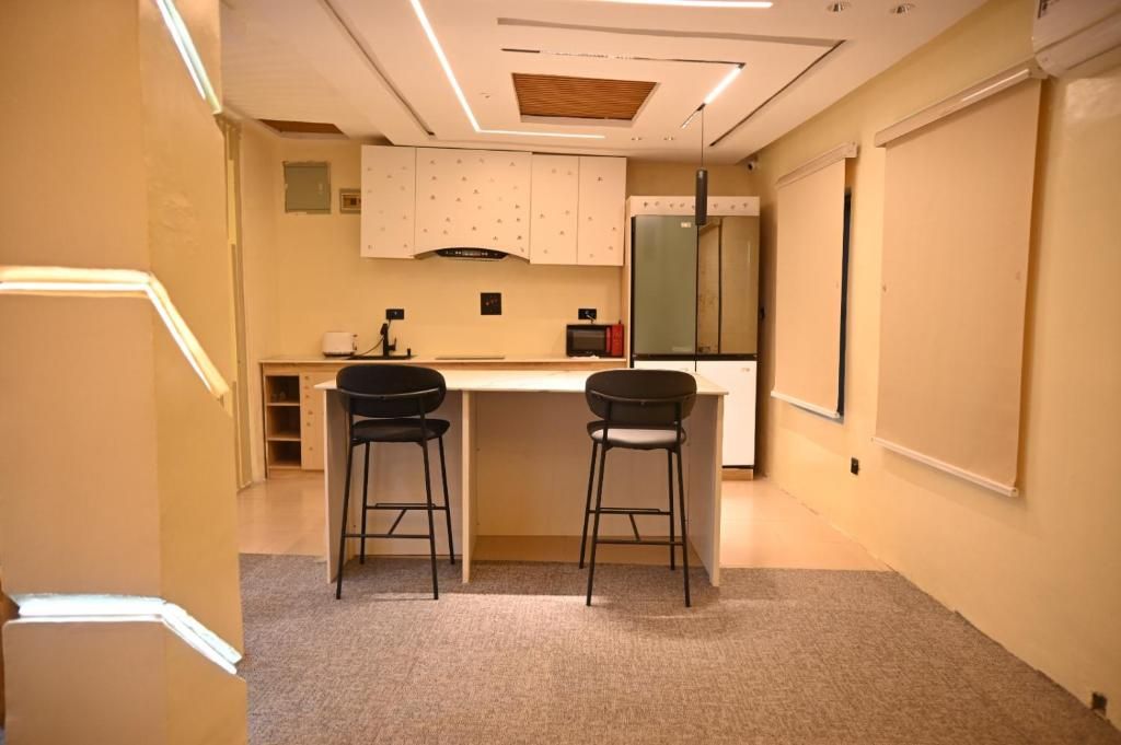 A small kitchenette with a refrigerator, a microwave, and a stove. There are two stools and a small table.