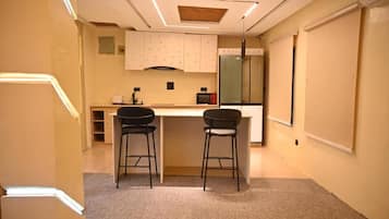 A small kitchenette with a refrigerator, a microwave, and a stove. There are two stools and a small table.