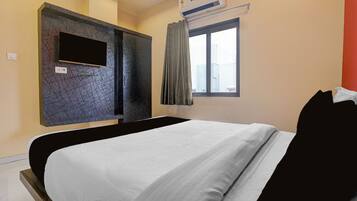 Habitación de hotel con cama, televisor montado, equipo de aire acondicionado y ventana con cortinas.