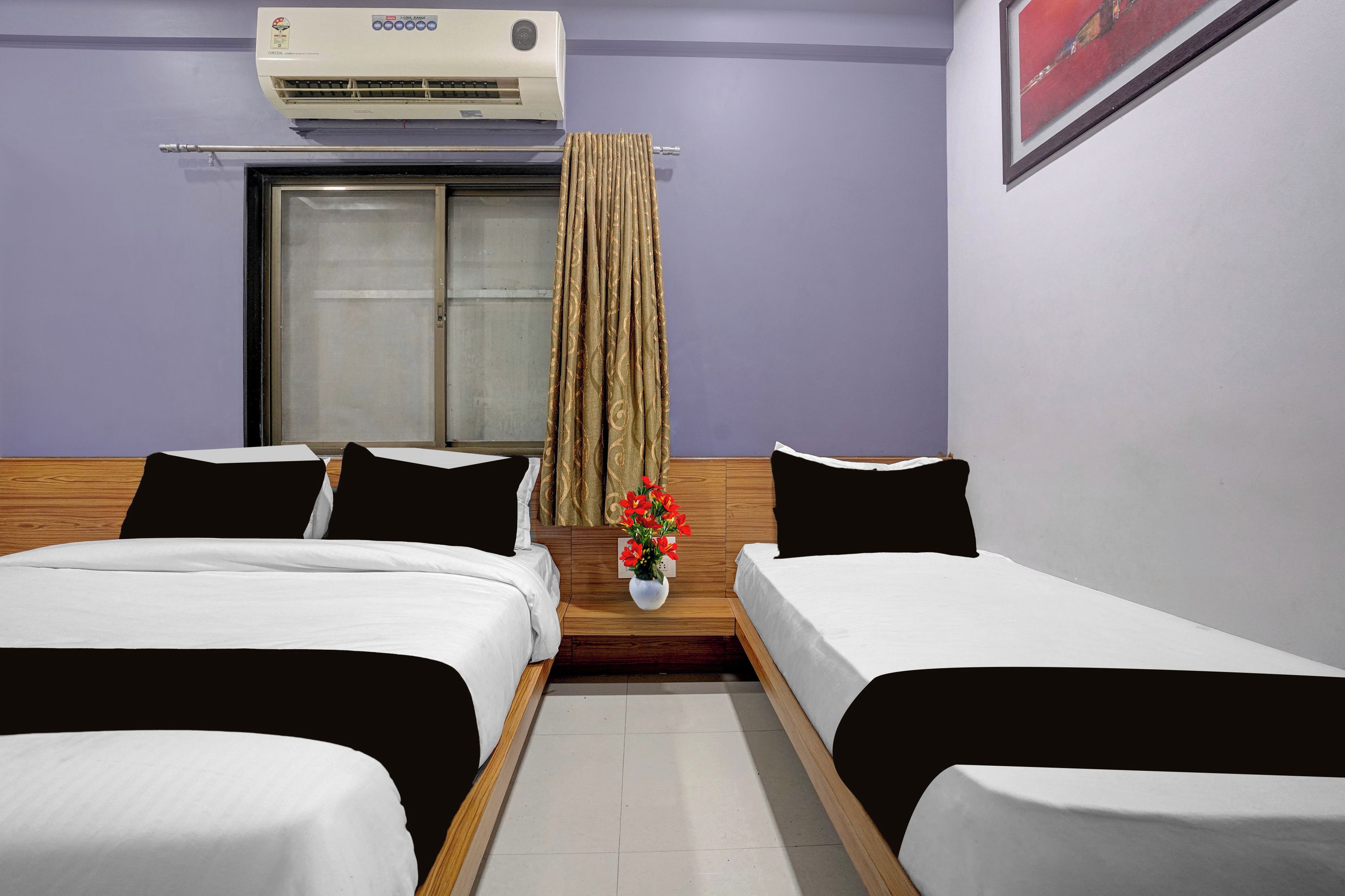 Habitación de hotel con dos camas individuales, una ventana con cortinas, un aire acondicionado instalado en la pared y una mesita con un florero.