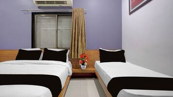 Habitación de hotel con dos camas individuales, una ventana con cortinas, un aire acondicionado instalado en la pared y una mesita con un florero.