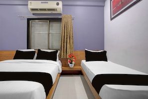 A hotel room with two single beds, a window with curtains, a wall-mounted air conditioner, and a small table with a vase of flowers. - Hotel O Saibaba Temple Shirdi (Shirdi)