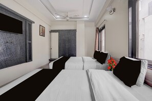 Habitación de hotel con dos camas, un ventilador de techo, una ventana con cortinas y una pared con diseño geométrico.