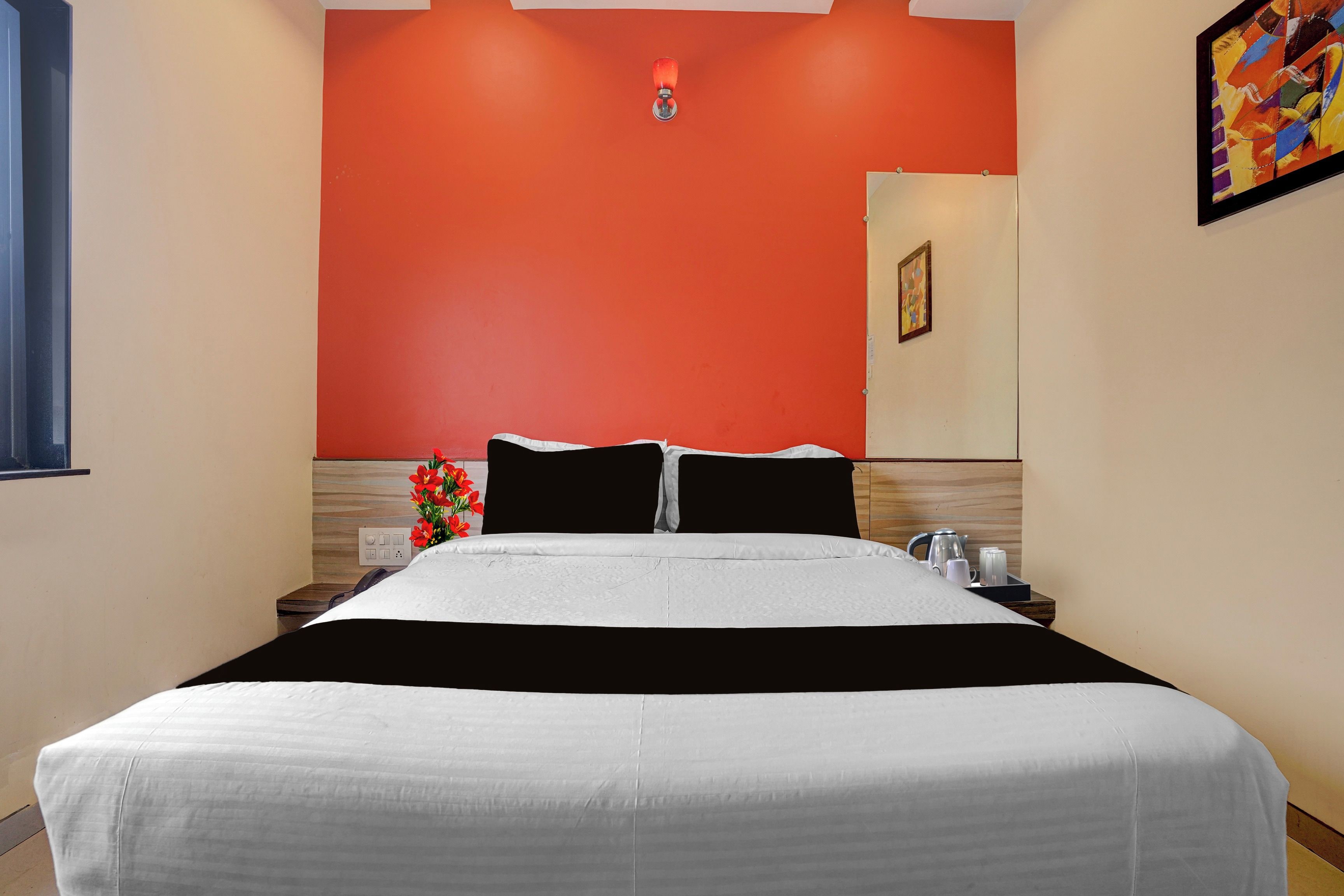 Una habitación de hotel con una cama, una mesita de noche, un florero con flores y un cuadro en la pared.