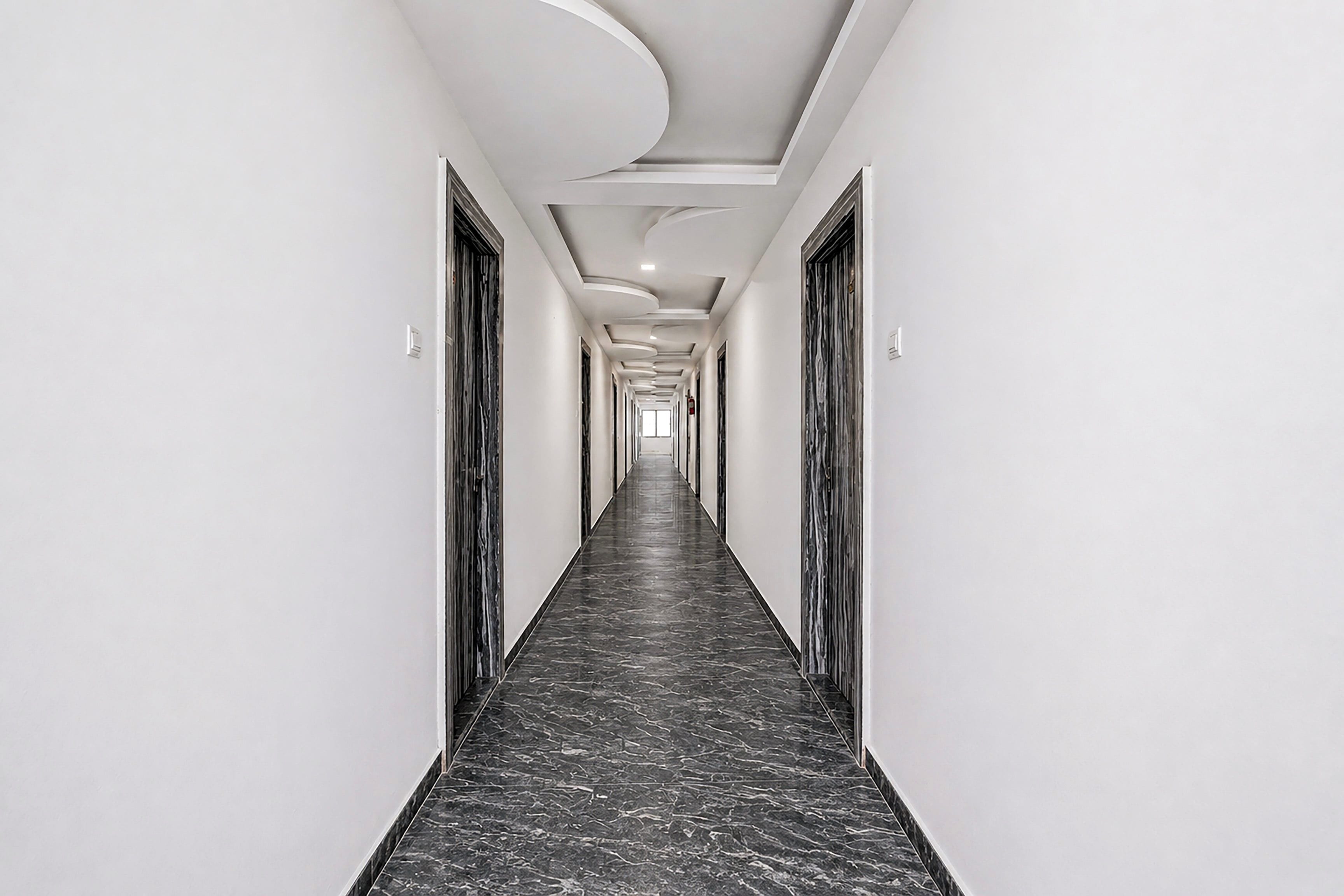 A long, narrow hallway with a marble floor and white walls, leading to a door at the end.