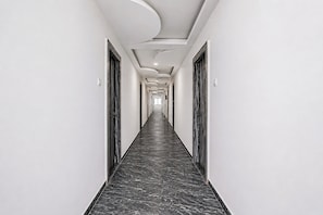 Un long couloir étroit, doté d’un sol en marbre et de murs blancs, qui mène à une porte au fond.