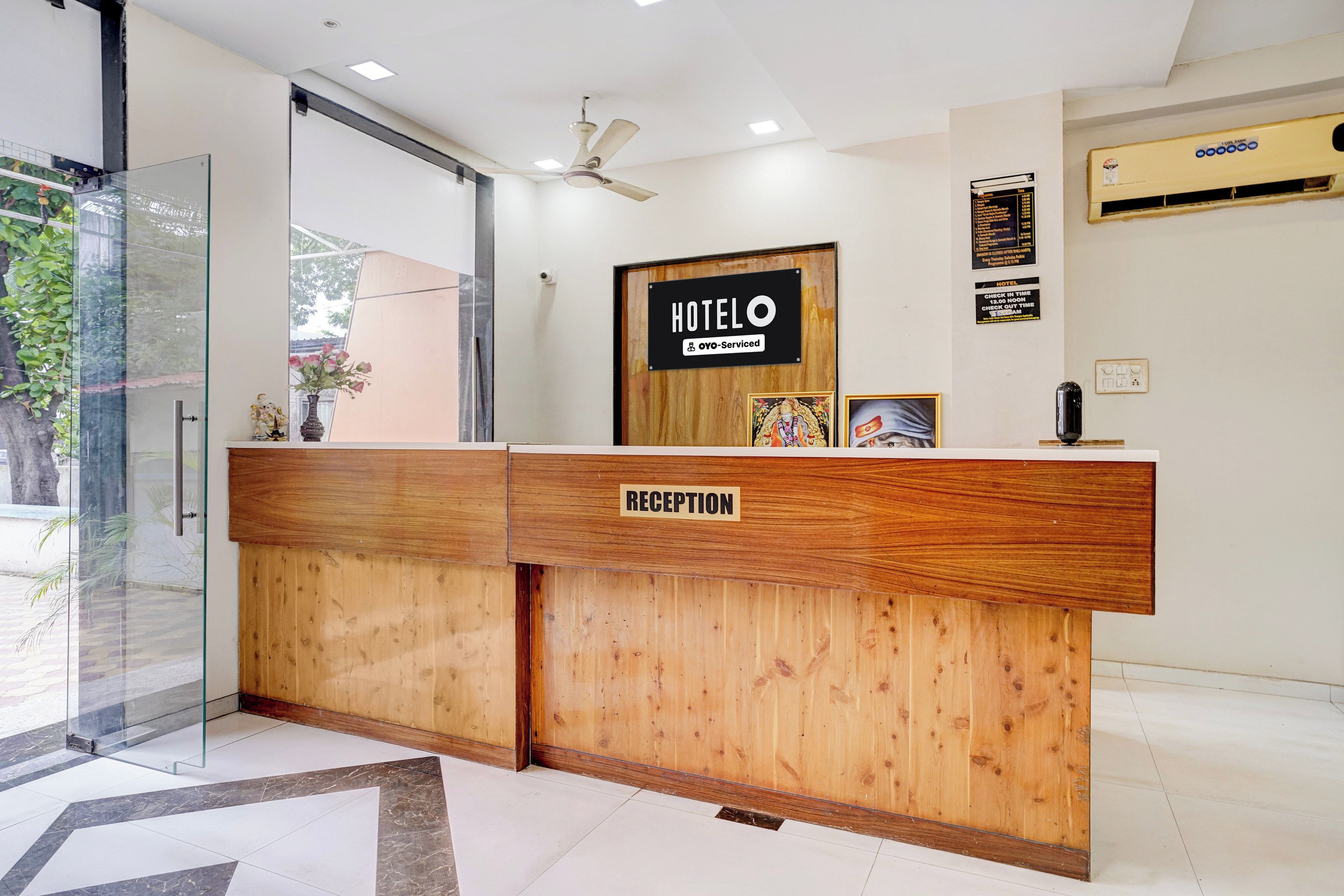 A hotel reception desk with a wooden finish, a reception sign, and a check-in/out time notice.