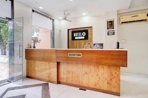 Un comptoir d’accueil d’hôtel avec un revêtement en bois, une enseigne indiquant « réception » et un panneau indiquant les heures d’arrivée et de départ.