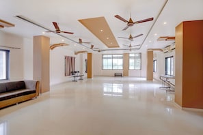Un hall d’hôtel spacieux, doté de plusieurs ventilateurs de plafond, de grandes fenêtres, d’un coin salon avec un canapé et une petite table.