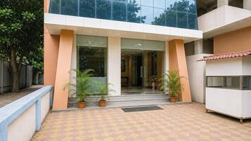 A building entrance with a tiled patio, potted plants, and a glass door leading inside.