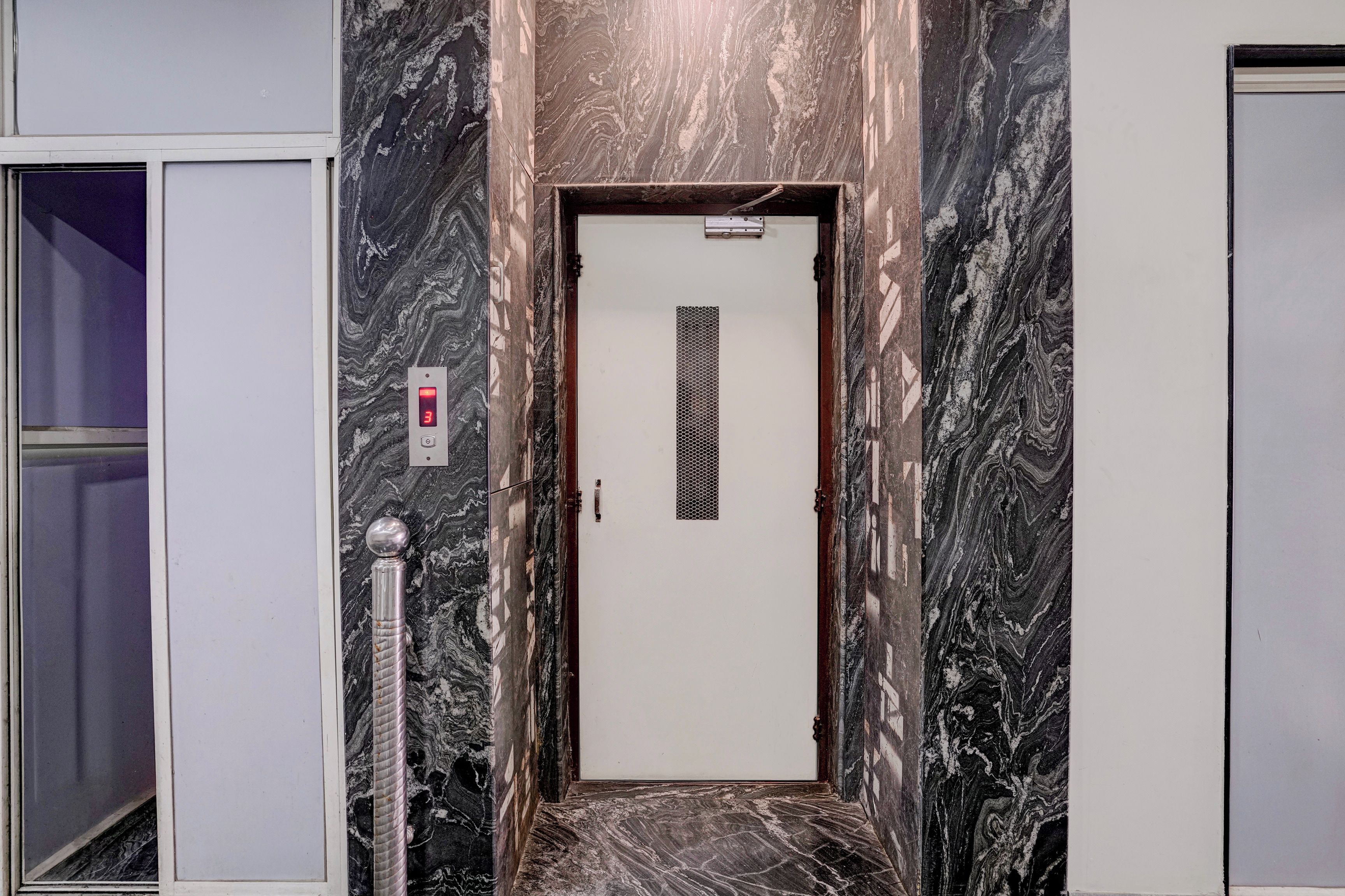 Un pasillo con pared de mármol, una puerta con pantalla digital y un poste de metal.