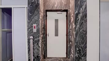 Un pasillo con pared de mármol, una puerta con pantalla digital y un poste de metal.