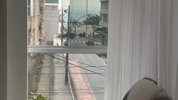 Quarto com vista para a rua, uma cadeira e um vaso com planta.
