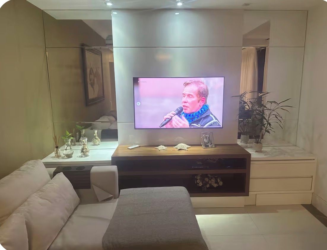 Uma sala de estar moderna com televisão de tela plana na parede, um sofá, uma mesa de centro e objetos decorativos.
