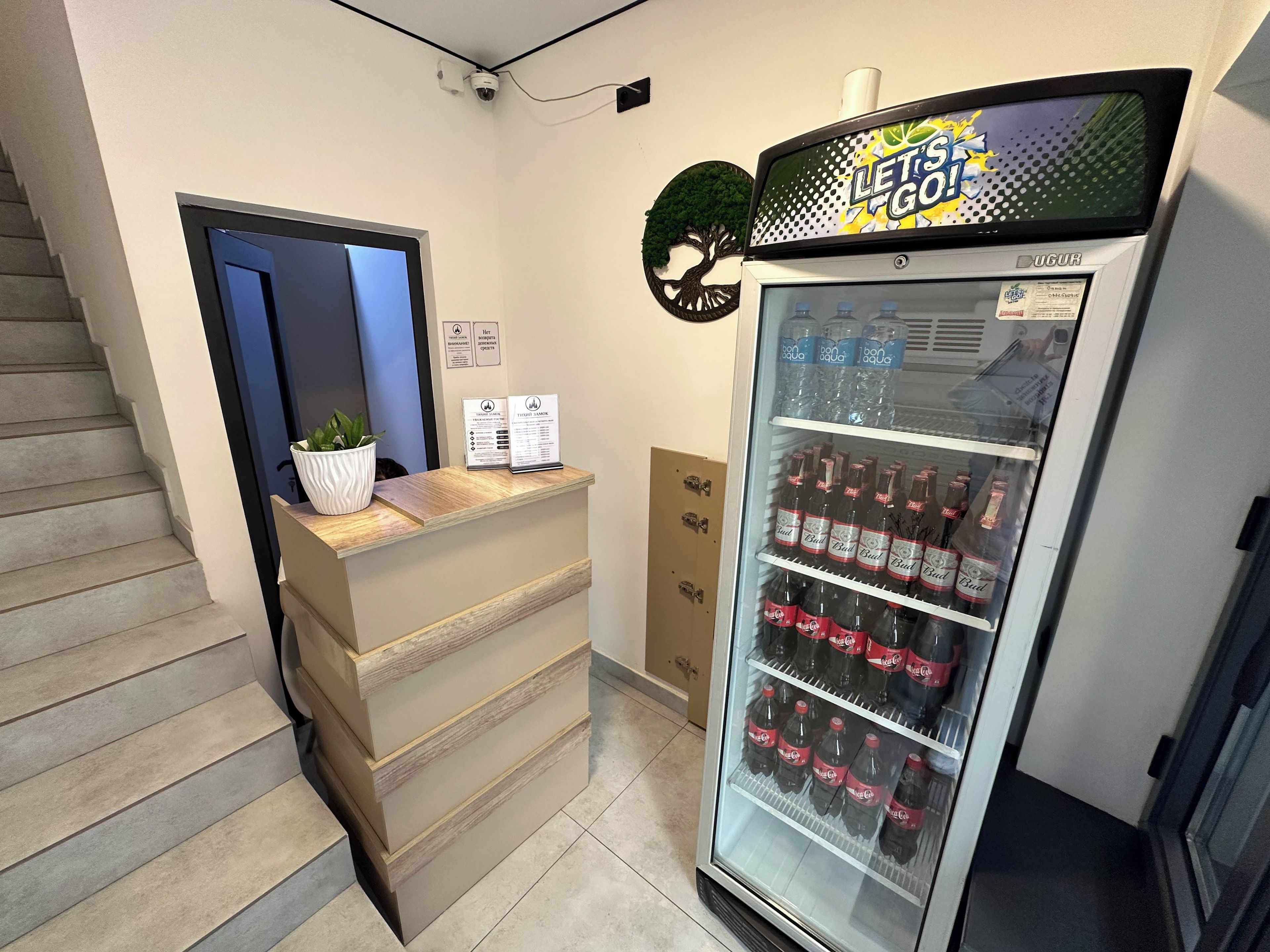 A reception desk with a potted plant, a refrigerator stocked with beverages, and a staircase.