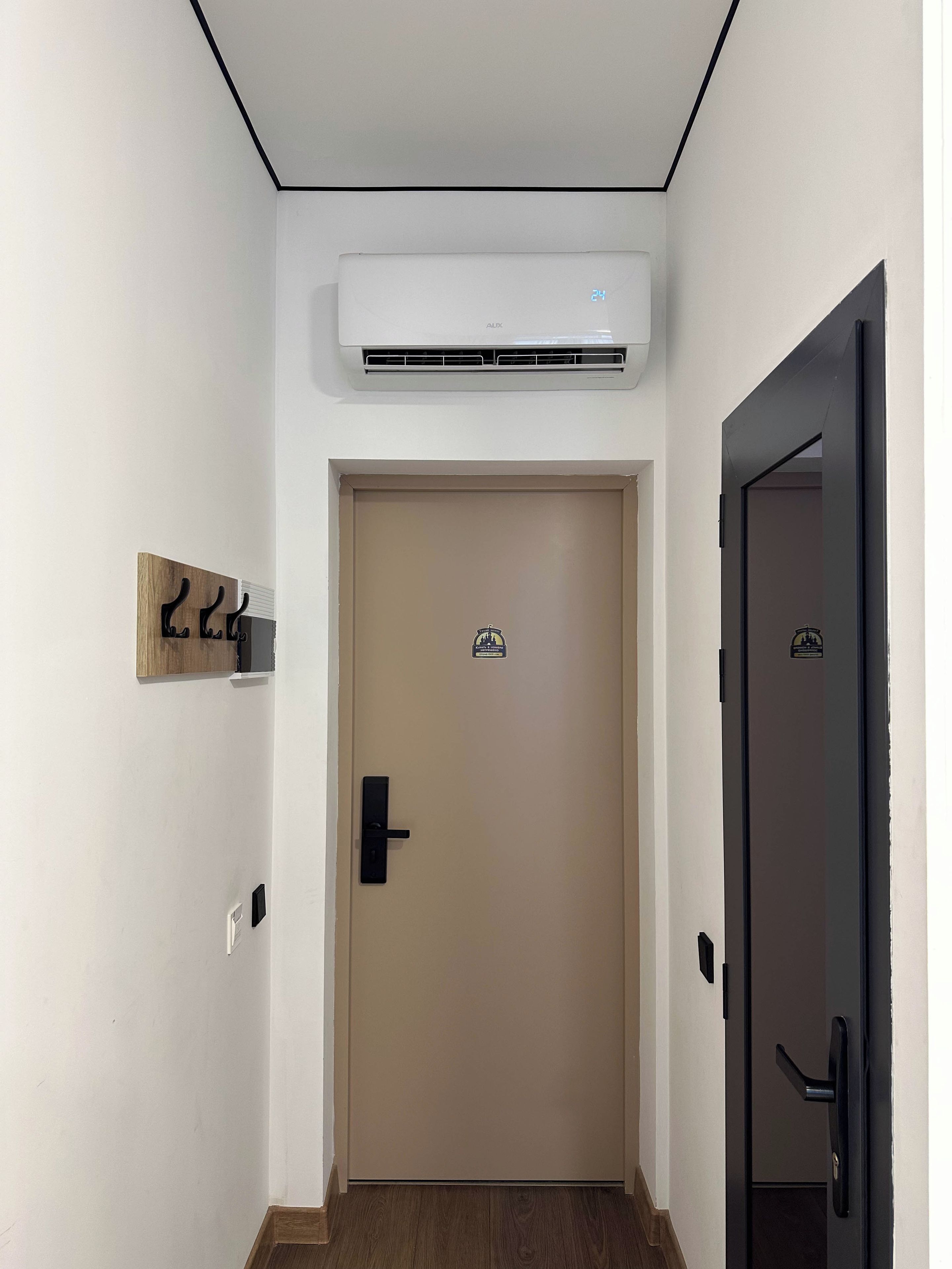 Un corridoio con una porta beige, una porta nera e un condizionatore d'aria a parete.