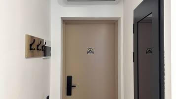 Un pasillo con una puerta color beige, una puerta negra y un equipo de aire acondicionado instalado en la pared.