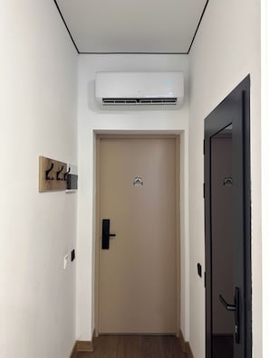 Un pasillo con una puerta color beige, una puerta negra y un equipo de aire acondicionado instalado en la pared.