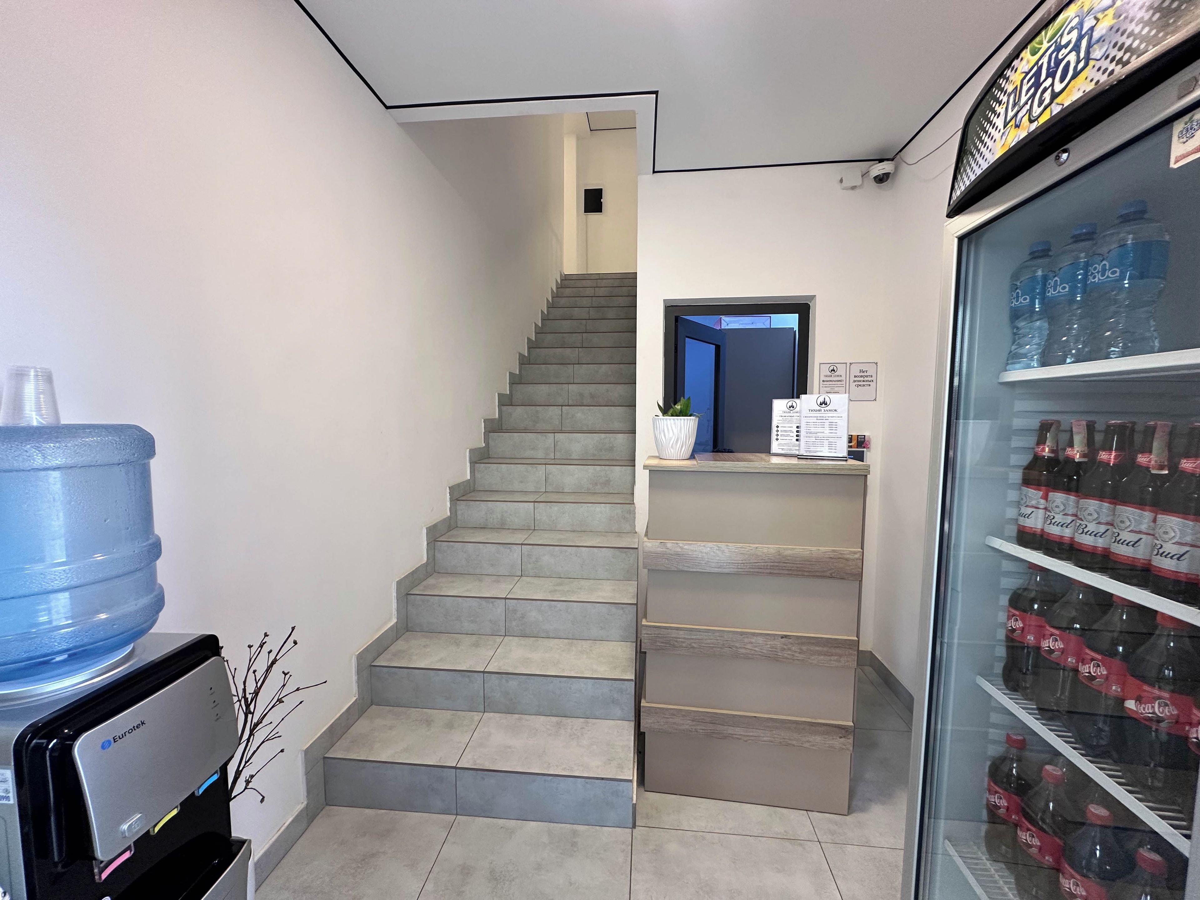 Una escalera que lleva a una puerta, un dispensador de agua y un refrigerador lleno de bebidas.