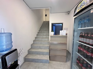 Una escalera que lleva a una puerta, un dispensador de agua y un refrigerador lleno de bebidas.