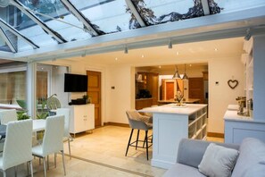 A modern kitchen with a central island, a dining area with white chairs, and a living space with a sofa. - Luxury6 Bed Villa-HotTub-FootballPitch-DogFriendly (Poole)