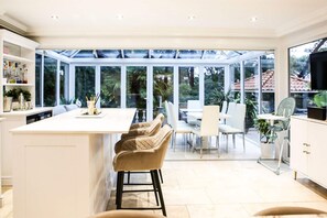 A modern kitchen with a large island, bar stools, and a dining area with chairs and a table. - Luxury6 Bed Villa-HotTub-FootballPitch-DogFriendly (Poole)