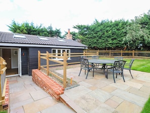 A patio area with a table and chairs, a brick wall, and a wooden fence. - Bramley Cottage (Beccles)