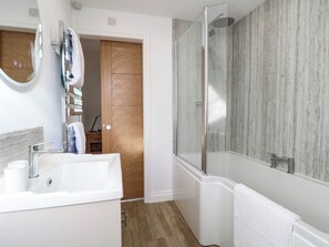 A modern bathroom with a glass shower enclosure, a white sink, and a wooden door. - Bramley Cottage (Beccles)