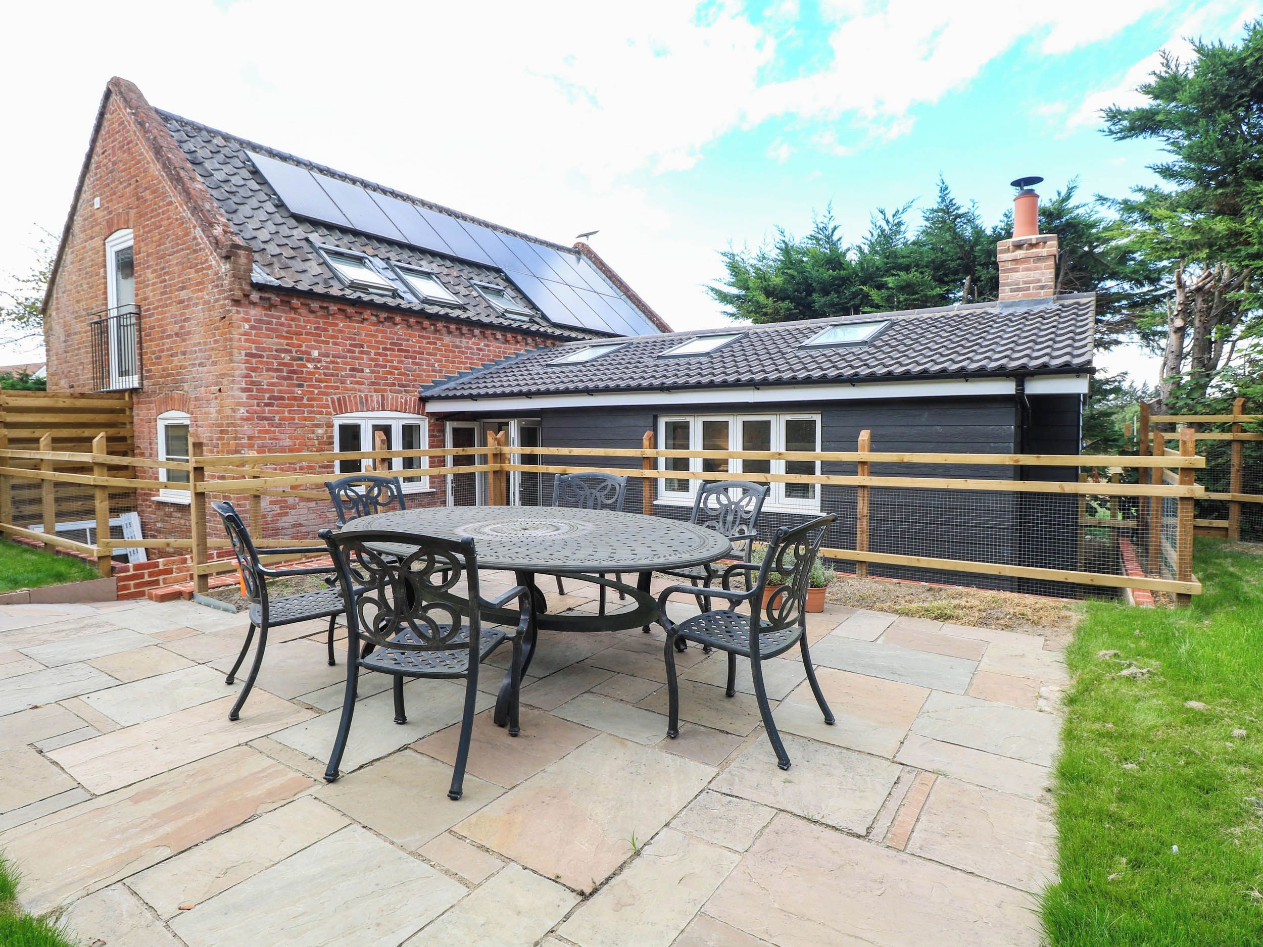 A brick house with a tiled roof, a fenced garden, and a patio with a table and chairs.