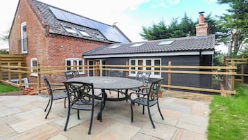 A brick house with a tiled roof, a fenced garden, and a patio with a table and chairs.