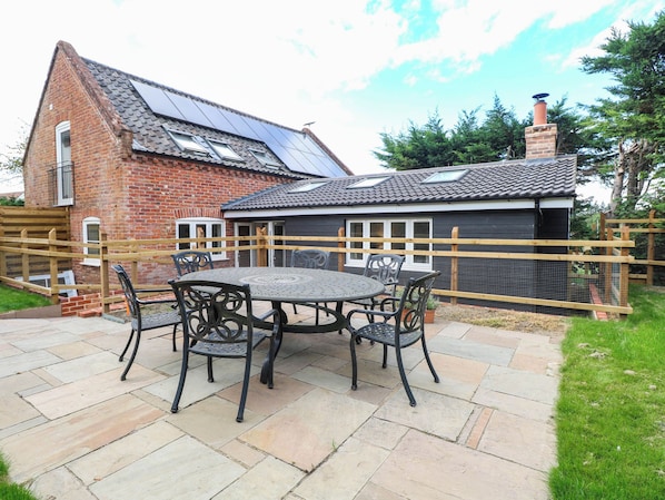 A brick house with a tiled roof, a fenced garden, and a patio with a table and chairs. - Bramley Cottage (Beccles)