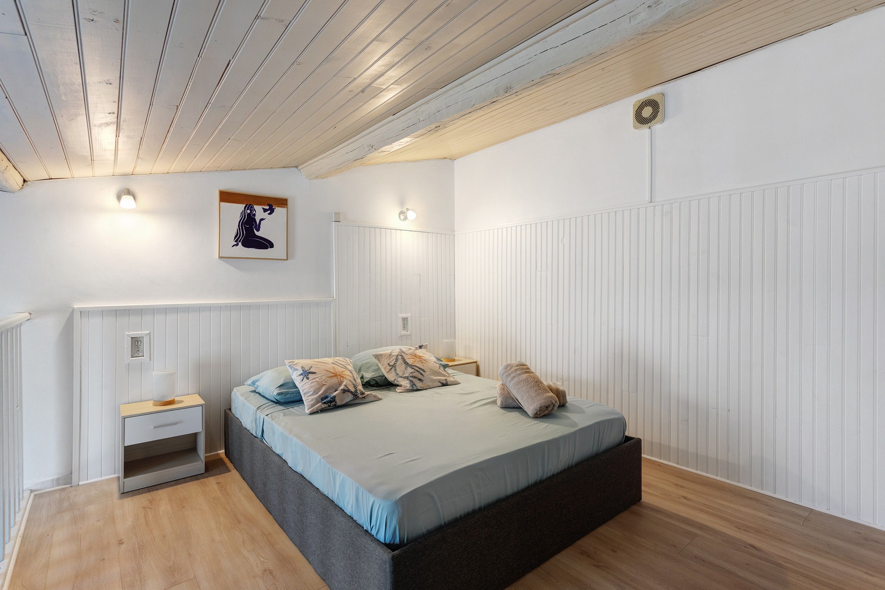 Een slaapkamer met een bed, nachtkastjes, een wandlamp en een plafondventilator.