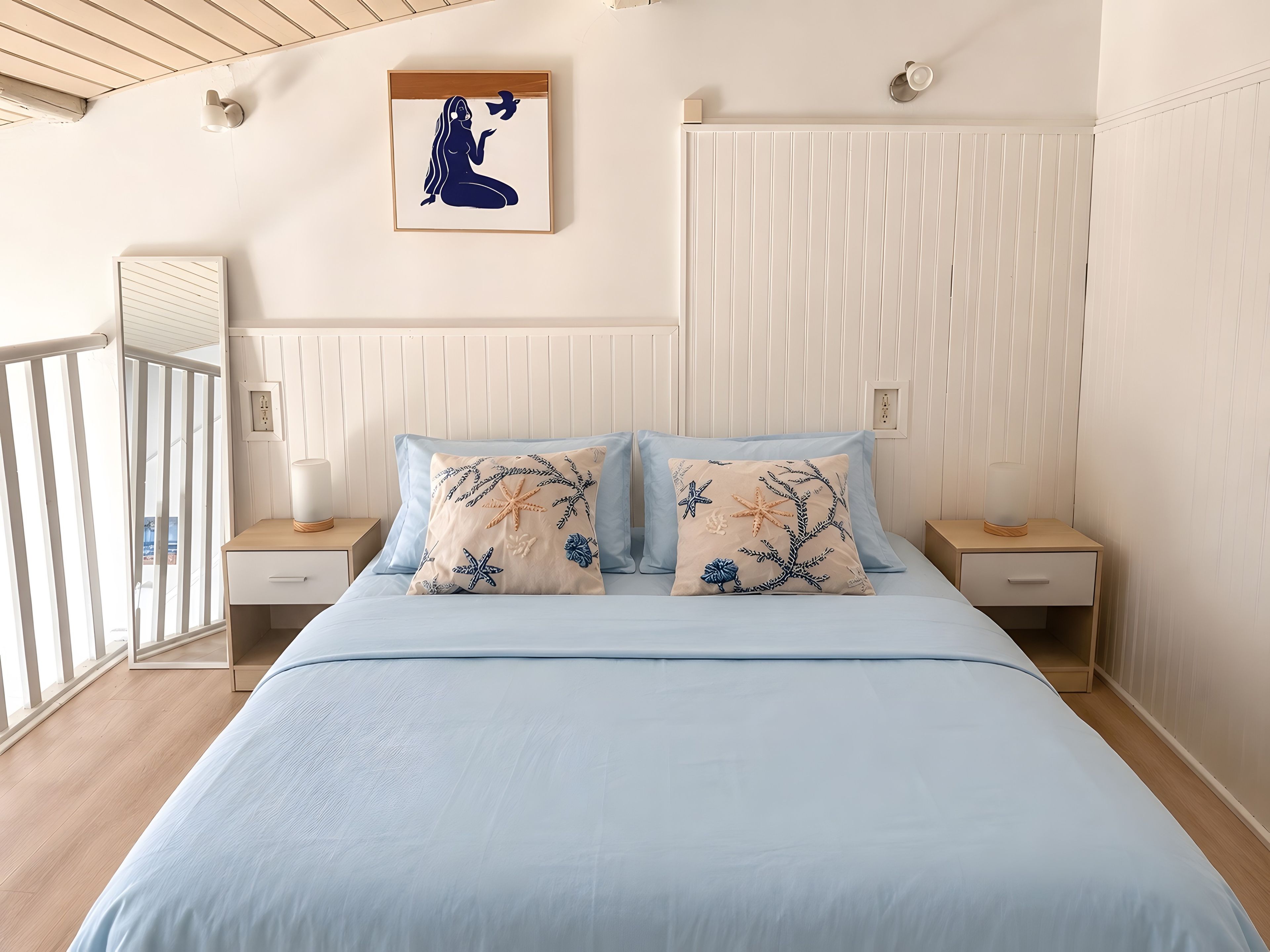 Une chambre à coucher comprenant un lit, deux tables de chevet, une commode, une lampe fixée au mur, un tableau encadré et une fenêtre donnant sur un paysage.
