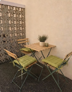 A small outdoor seating area with a wooden table and chairs, a potted plant, and a decorative wall panel.