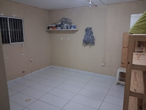 A room with a tiled floor, a window with bars, a shelf with various items, and a wall-mounted decorative piece.